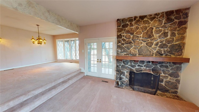 unfurnished living room with a stone fireplace, french doors, carpet floors, and a chandelier