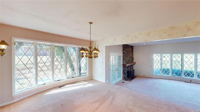 unfurnished living room featuring a stone fireplace, light carpet, plenty of natural light, and a chandelier