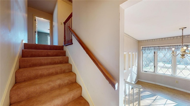 staircase with wood-type flooring and a notable chandelier