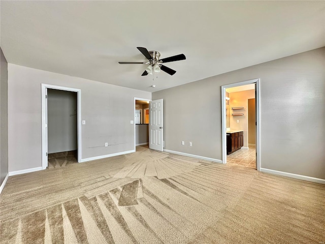 unfurnished bedroom featuring light colored carpet, ceiling fan, a spacious closet, connected bathroom, and a closet