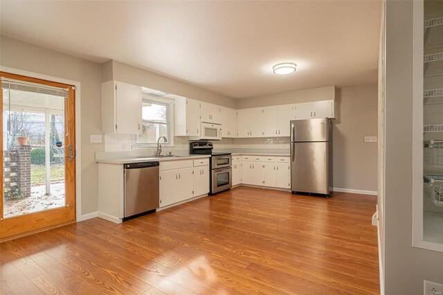 kitchen with stainless steel appliances, a wealth of natural light, white cabinets, and light hardwood / wood-style floors