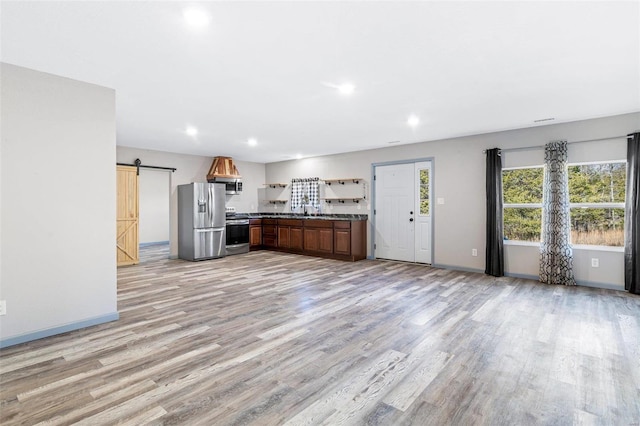 kitchen featuring light stone countertops, sink, stainless steel appliances, a barn door, and light hardwood / wood-style flooring