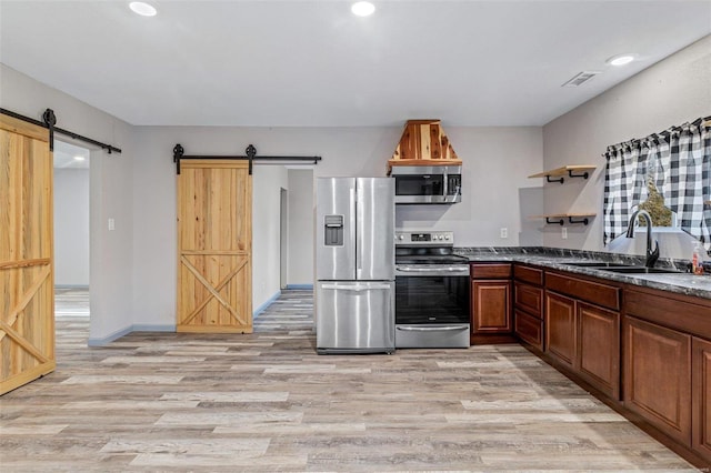 kitchen featuring a barn door, sink, light hardwood / wood-style floors, and appliances with stainless steel finishes