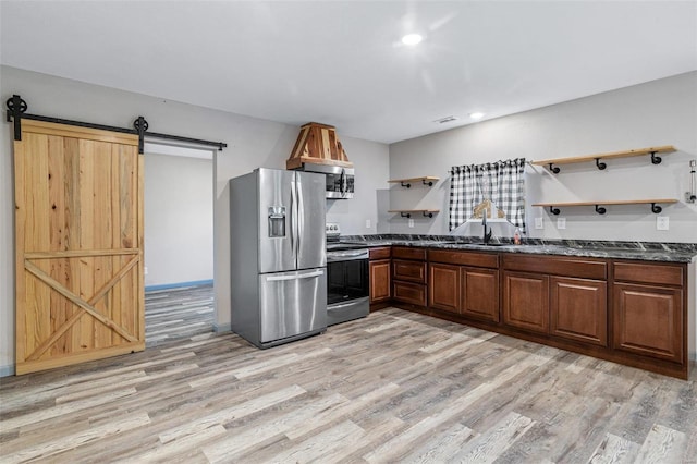 kitchen featuring appliances with stainless steel finishes, a barn door, light hardwood / wood-style flooring, and dark stone countertops