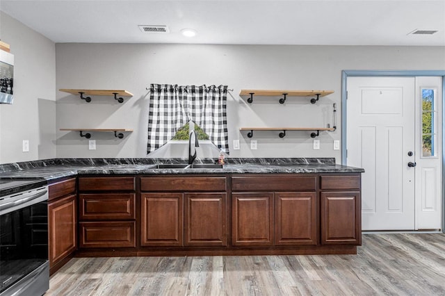 kitchen with black electric range, light hardwood / wood-style floors, dark stone counters, and sink