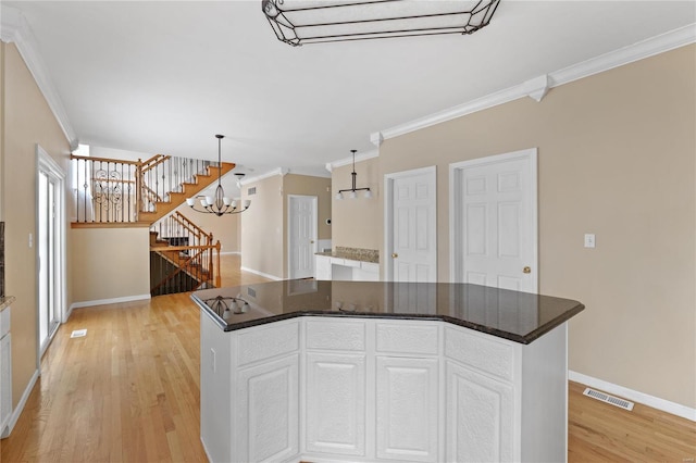 kitchen featuring white cabinetry, a center island, hanging light fixtures, crown molding, and light wood-type flooring