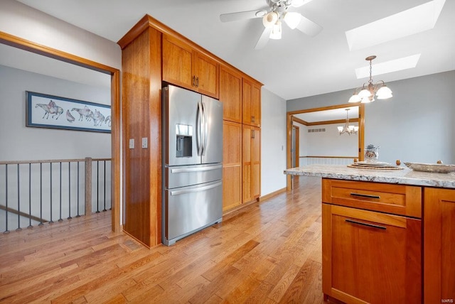 kitchen featuring pendant lighting, ceiling fan with notable chandelier, stainless steel refrigerator with ice dispenser, a skylight, and light wood-type flooring