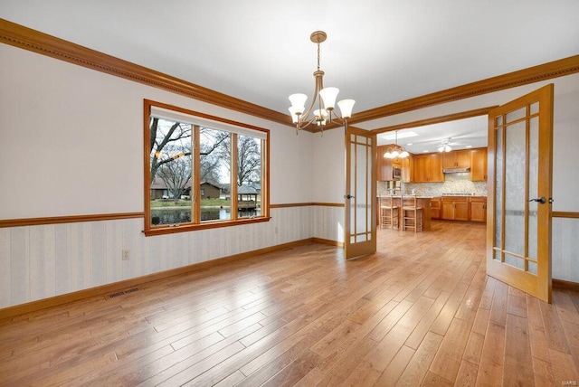 unfurnished dining area with french doors, ceiling fan with notable chandelier, light hardwood / wood-style floors, and crown molding