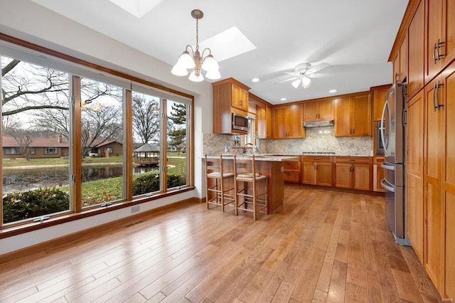 kitchen featuring a skylight, backsplash, light wood-type flooring, a breakfast bar, and appliances with stainless steel finishes