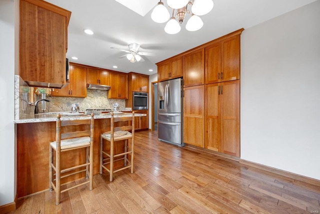 kitchen featuring a breakfast bar area, light hardwood / wood-style flooring, tasteful backsplash, kitchen peninsula, and stainless steel appliances