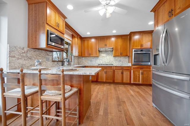 kitchen featuring backsplash, light hardwood / wood-style flooring, a kitchen bar, kitchen peninsula, and stainless steel appliances