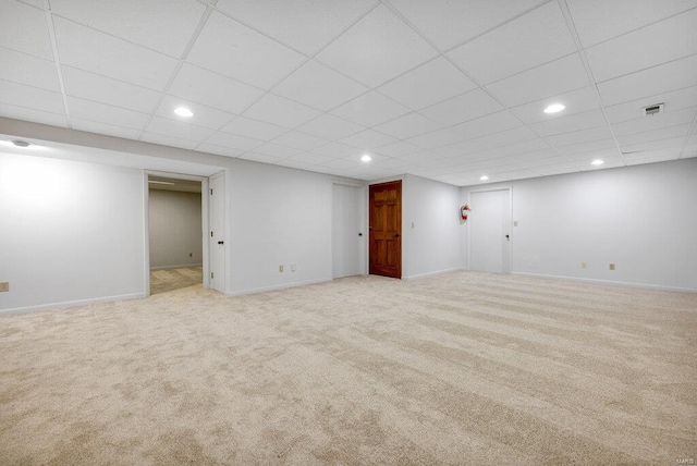 basement with a paneled ceiling and light colored carpet