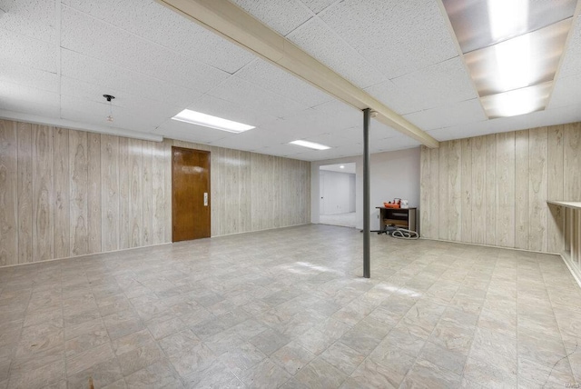 basement with a drop ceiling and wood walls