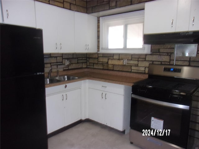 kitchen with under cabinet range hood, stainless steel range with gas stovetop, freestanding refrigerator, white cabinets, and a sink