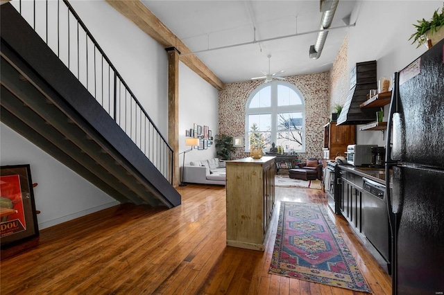 kitchen featuring brick wall, a high ceiling, hardwood / wood-style flooring, a notable chandelier, and black appliances