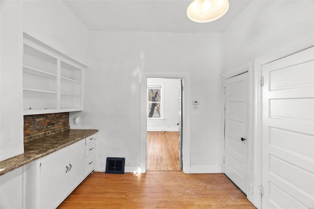 kitchen with white cabinets, light wood-type flooring, tasteful backsplash, dark stone counters, and built in shelves