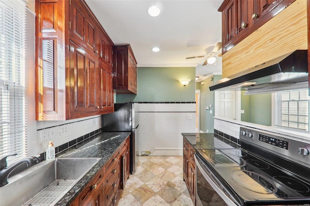 kitchen with range with electric cooktop, dark stone counters, ceiling fan, sink, and wall chimney range hood