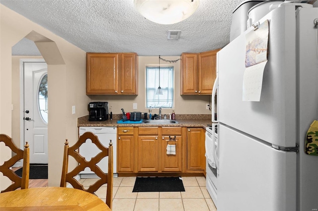 kitchen featuring dark stone counters, a textured ceiling, white appliances, sink, and light tile patterned flooring