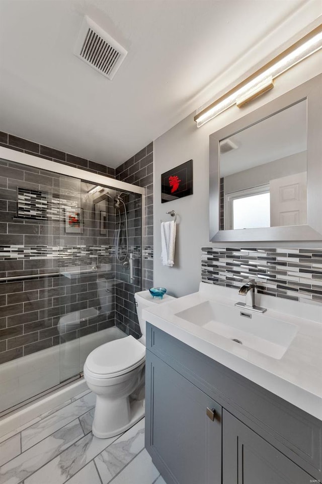 bathroom featuring vanity, toilet, a shower with shower door, and tasteful backsplash