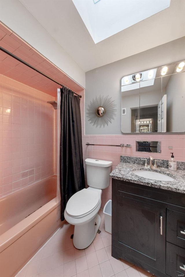 full bathroom featuring a skylight, vanity, shower / bath combo with shower curtain, tile walls, and toilet