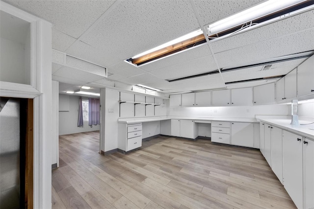 unfurnished office with a drop ceiling, built in desk, and light wood-type flooring