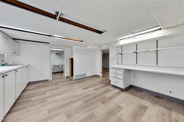 basement with sink, built in desk, a drop ceiling, and light wood-type flooring