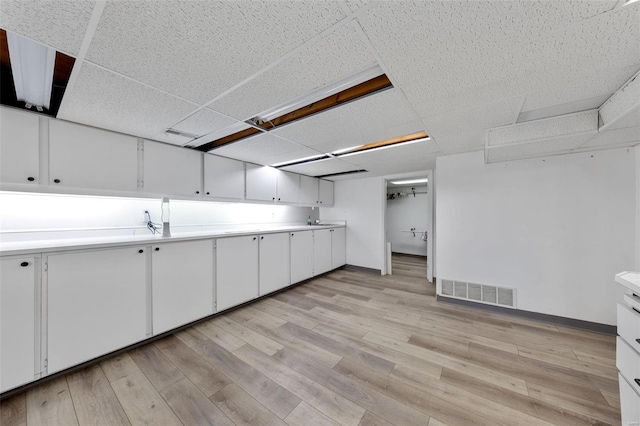 kitchen featuring white cabinetry, a drop ceiling, and light wood-type flooring