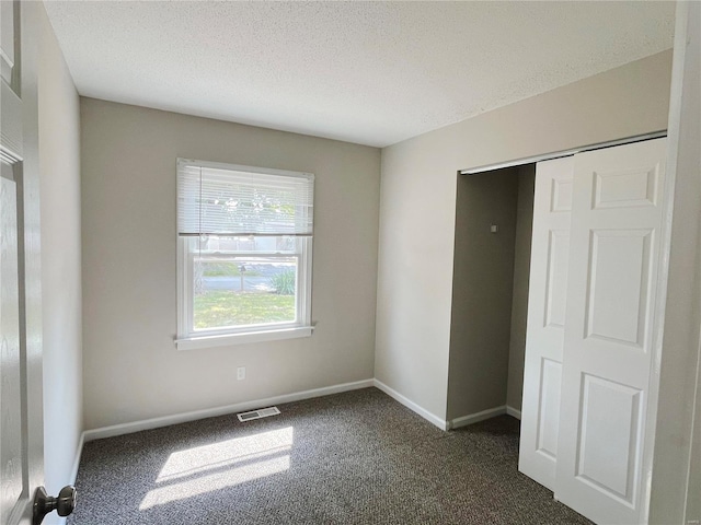 unfurnished bedroom featuring a closet, a textured ceiling, and dark colored carpet