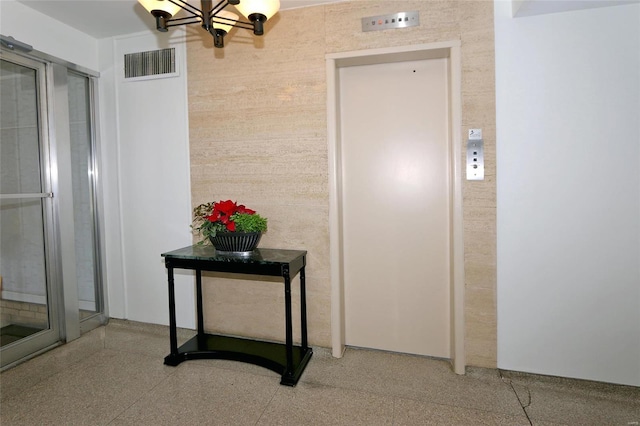 hallway with elevator and a notable chandelier