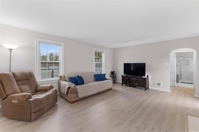 living area with visible vents, light wood-style floors, arched walkways, and baseboards