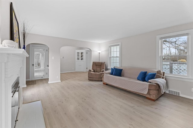 living area with arched walkways, visible vents, light wood-type flooring, and baseboards