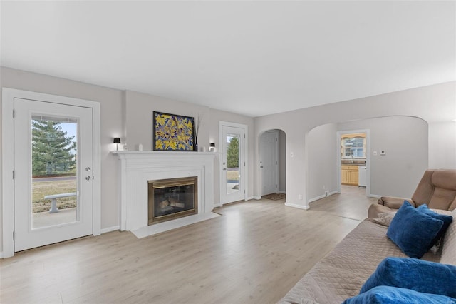 living room with arched walkways, a fireplace with flush hearth, light wood-type flooring, and baseboards