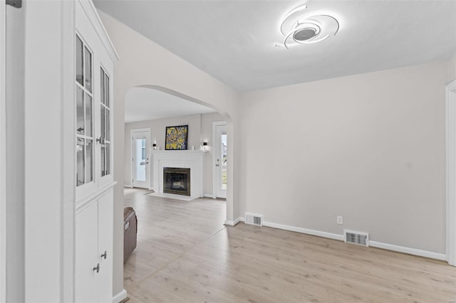 living area featuring light wood-style floors, a fireplace with flush hearth, arched walkways, and visible vents