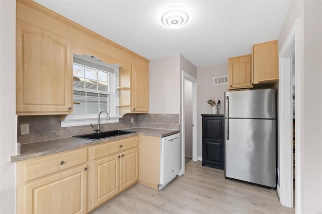 kitchen with a sink, dishwasher, light brown cabinets, and freestanding refrigerator