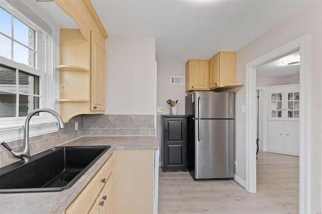 kitchen with light brown cabinets, visible vents, freestanding refrigerator, and a sink