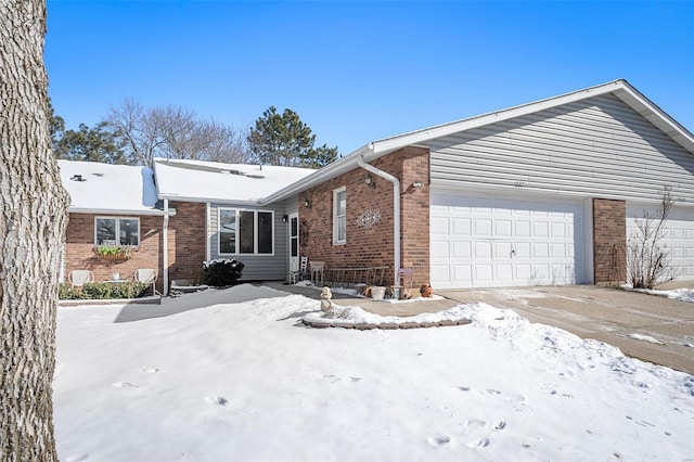 view of snowy exterior featuring an attached garage, brick siding, and driveway