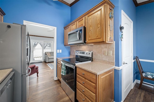 kitchen with crown molding, dark wood-type flooring, light countertops, decorative backsplash, and appliances with stainless steel finishes