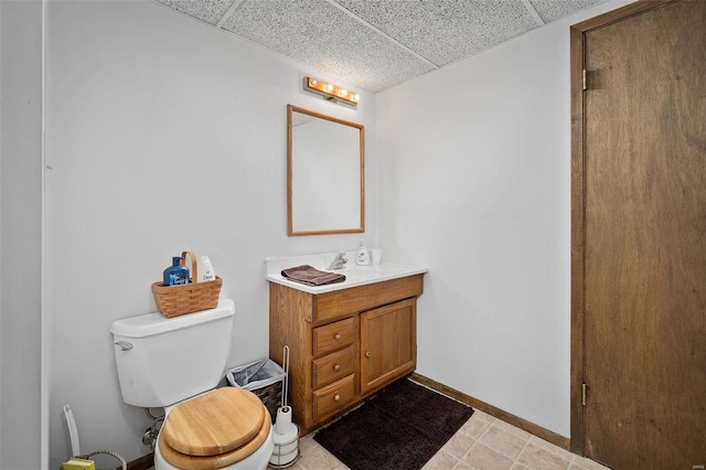 bathroom with baseboards, a paneled ceiling, toilet, and vanity