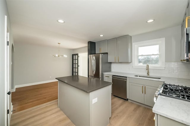 kitchen featuring appliances with stainless steel finishes, light wood-type flooring, sink, a center island, and hanging light fixtures