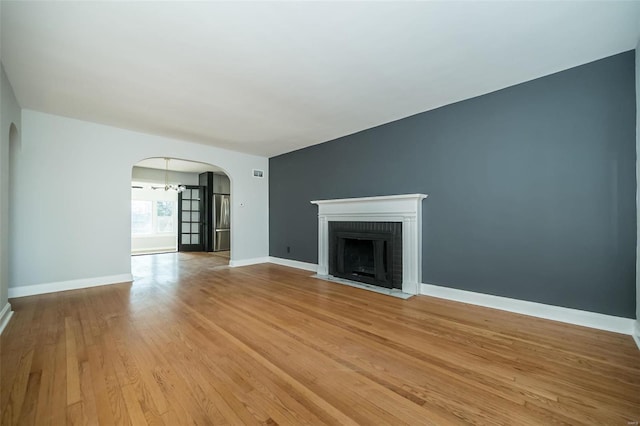 unfurnished living room with an inviting chandelier, light hardwood / wood-style floors, and a brick fireplace