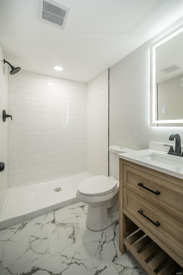 bathroom with tiled shower, vanity, and toilet