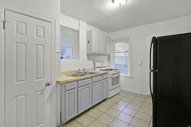 kitchen featuring black refrigerator, sink, gray cabinets, a textured ceiling, and gas range gas stove