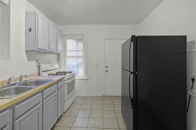 kitchen with gray cabinets, black fridge, white gas range, and sink