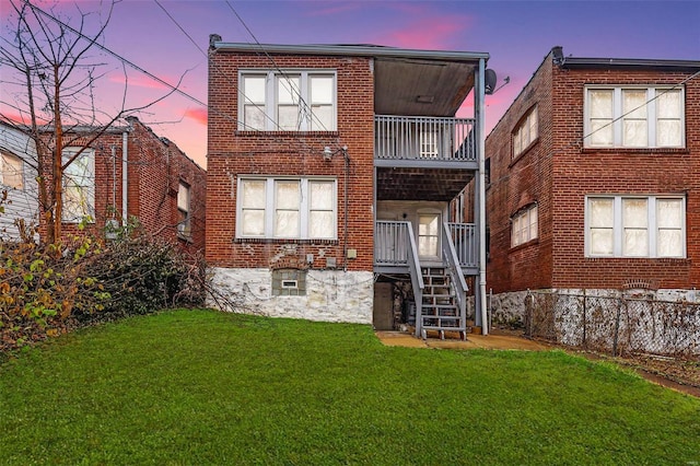 back house at dusk with a yard and a balcony