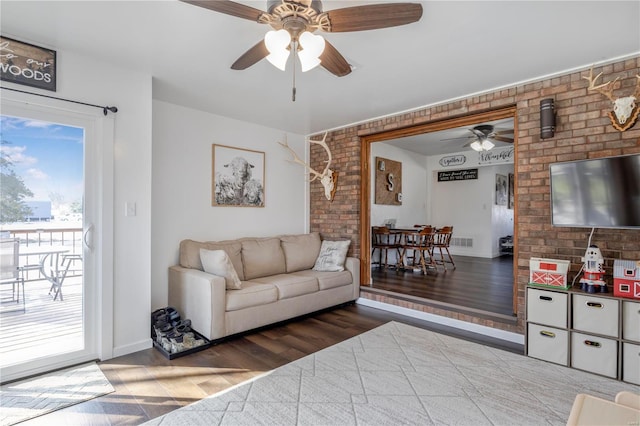 living area with visible vents, wood finished floors, ceiling fan, and brick wall