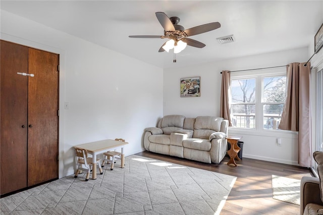 living room featuring baseboards, visible vents, light wood-type flooring, and ceiling fan