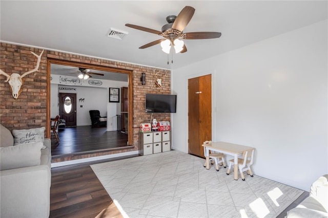 living room featuring visible vents, brick wall, ceiling fan, and wood finished floors