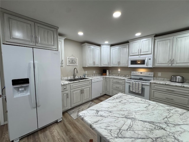 kitchen featuring white appliances, white cabinets, sink, light stone counters, and wood-type flooring