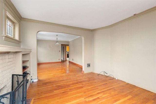 empty room featuring built in shelves, light wood-type flooring, a brick fireplace, and ornamental molding