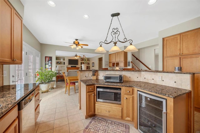 kitchen featuring ceiling fan, beverage cooler, dark stone countertops, decorative light fixtures, and appliances with stainless steel finishes